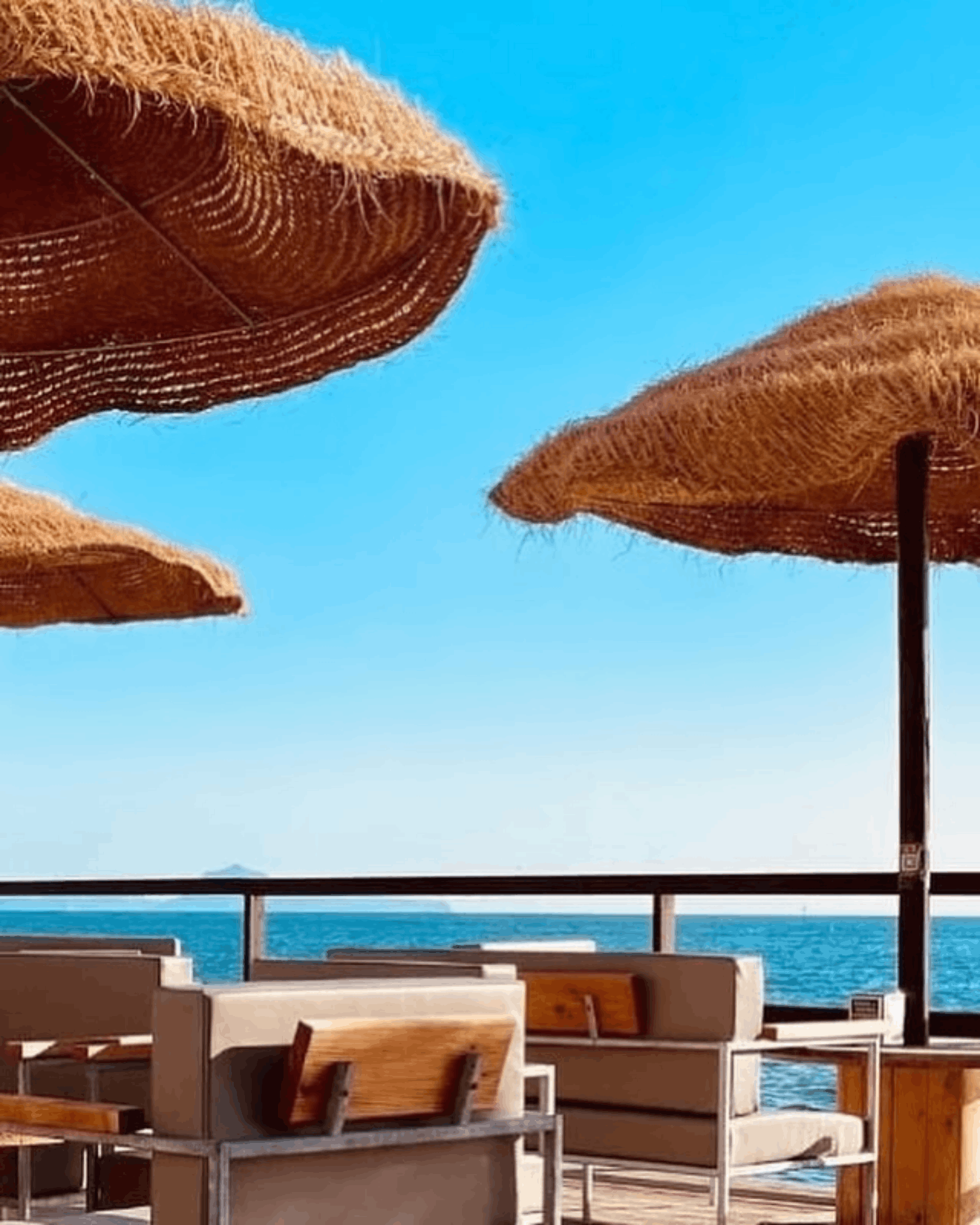 Ombrelloni di paglia e lettini del solarium del Noa Beach con vista sul golfo